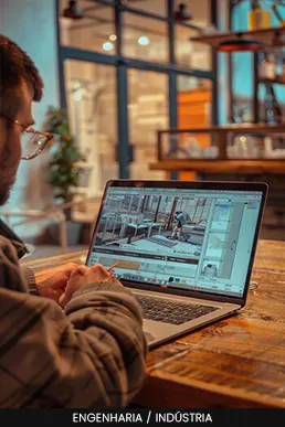Homem operando software de modelagem ou monitoramento industrial em um notebook sobre mesa de madeira.