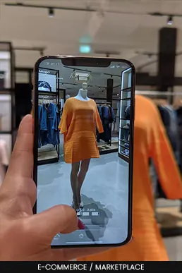 Smartphone exibindo aplicativo de compras com realidade aumentada em uma loja de roupas física.