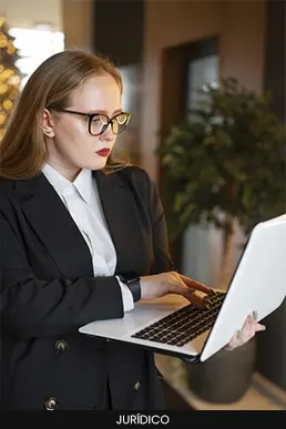 Mulher com óculos vestindo traje formal e utilizando um notebook branco em ambiente corporativo.
