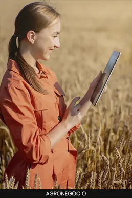 Mulher em campo de plantação de trigo utilizando um tablet para monitoramento agrícola.